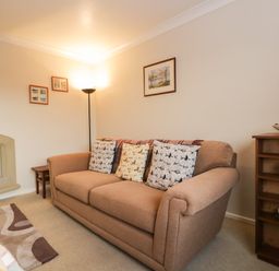 A living room with a beige sofa a floor lamp a fireplace and framed pictures on the wall at Marsh Garth in Kirkby-In-Furness