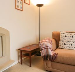 A living room corner with a beige sofa and patterned cushions next to a wooden side table and a tall floor lamp at Marsh Garth in Kirkby-In-Furness