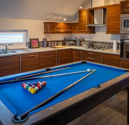 A kitchen with wooden cabinets a blue pool table and billiard cues at Lakeland Lodge in Carnforth