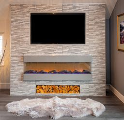 A fireplace with stacked firewood below and a television mounted above in a room with a soft rug on the floor at Lakeland Lodge in Carnforth