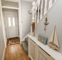 A hallway with a white front door a wooden floor stairs with a gray carpet and nautical decorations at Greengate in Tenby