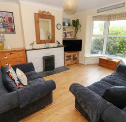 A living room with two dark blue sofas a fireplace a wooden chest and a bay window with blinds at Greengate in Tenby