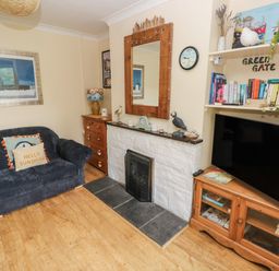A living room with a dark sofa a fireplace a large mirror and a wooden cabinet with a television at Greengate in Tenby