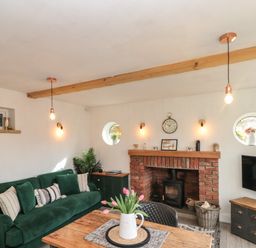 A living room with a green sofa a brick fireplace a wooden table and a television at Rosemary Cottage in Briggswath near Sleights