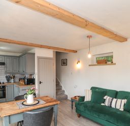 A kitchen and living area with a green sofa wooden table with flowers and wooden ceiling beams at Rosemary Cottage in Briggswath near Sleights