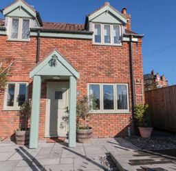 A brick house with a light green door and porch and several potted plants outside at Rosemary Cottage in Briggswath near Sleights