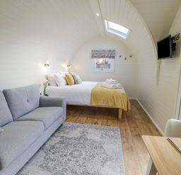 A bedroom with a bed and folded towels a grey sofa a patterned rug a wall-mounted TV and a dining table at Y Dderwen in Bontuchel near Ruthin