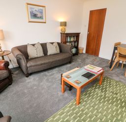 A sitting room with a grey sofa and green rug a wooden table and chairs at 8 Oaks Field Ambleside
