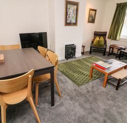 A living room with a dining table and chairs a television two armchairs a coffee table and a green rug at 8 Oaks Field in Ambleside