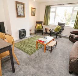 A living room with chairs a coffee table a green rug and a dining table at 8 Oaks Field in Ambleside