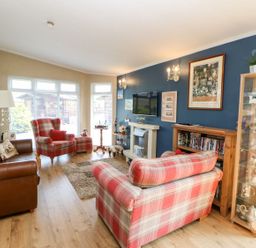A living room with a brown sofa and red plaid armchairs next to a blue wall with framed pictures at 6 Badgers Retreat in Tunstall near Richmond