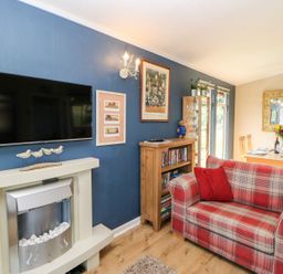 A living room with a plaid sofa a wooden cabinet a glass display unit a dining table and chairs with a large mirror at 6 Badgers Retreat in Tunstall near Richmond