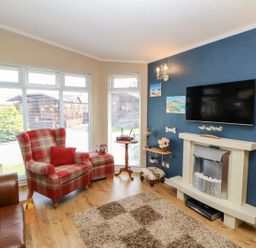 A living room with a plaid armchair, leather sofa, TV mounted above a fireplace, and large windows at 6 Badgers Retreat Tunstall near Richmond