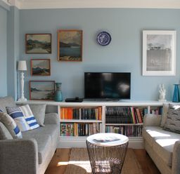 A sitting room with two sofas, a coffee table, a bookshelf with a TV on top, and paintings on the walls at 2 The Dunes Thorpeness