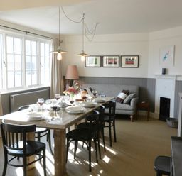 A dining room with a wooden table set with plates glasses and wine surrounded by black chairs and a gray sofa at 2 The Dunes Thorpeness
