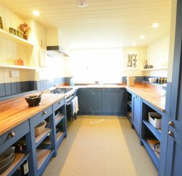A kitchen with blue cabinets wooden countertops open shelves and a stove at 2 The Dunes Thorpeness