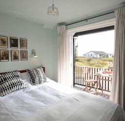 A bedroom with a bed and patterned pillows next to a balcony with a table and chairs at 2 The Dunes Thorpeness