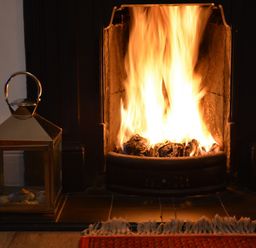 A burning fireplace with a lantern on the hearth and part of a red rug at Holmleigh Aldeburgh