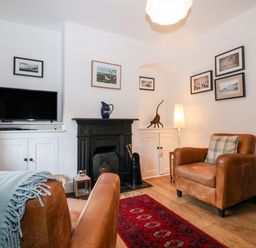 A living room with two brown leather armchairs a red patterned rug a black fireplace a television on a white cabinet and framed pictures on the walls at Holmleigh Aldeburgh in Aldeburgh