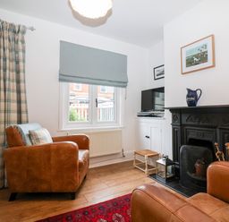 A sitting room with two brown leather armchairs a window with a blue roman blind a black fireplace with a blue jug on the mantle and a television on a white cabinet at Holmleigh Aldeburgh in Aldeburgh