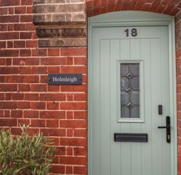 A green front door with the number 18 and a name plaque reading Holmleigh on a red brick wall at Holmleigh Aldeburgh