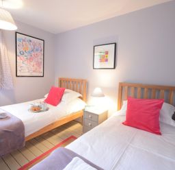 A bedroom with two single beds with pink pillows a bedside table a lamp and two framed pictures on the wall at Durdans Walberswick