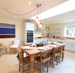 A kitchen with a wooden dining table set for six with wine glasses and plates at Durdans Walberswick