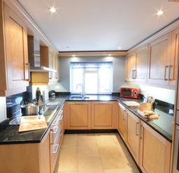A kitchen with wooden cabinets black countertops and cooking appliances at Bunny Cottage Aldeburgh
