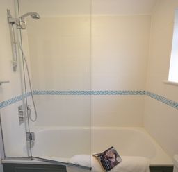 A bathroom with a bathtub shower with glass screen white tiles and a book on a white towel at Bunny Cottage Aldeburgh