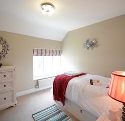 A bedroom with a single bed covered with white bedding and a red throw at Bunny Cottage Aldeburgh