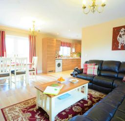 A living room with a black leather sofa and a wooden coffee table next to a dining table and wooden kitchen cabinets at Red Robin Whepstead in Wickhambrook near Bury St Edmunds