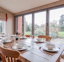 A dining room with a wooden table set for a meal at Holly Lodge in Aldeburgh