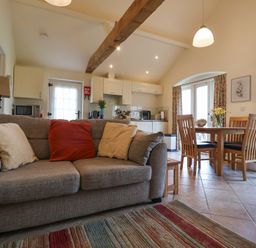 A living room with a sofa and cushions next to a dining table with chairs and a kitchen area with cabinets at Romulus in Larling near East Harling