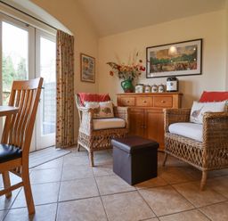 A seating area with two wicker armchairs with cushions and a small ottoman in front of a wooden sideboard with jars and a coffee machine at Romulus Larling near East Harling