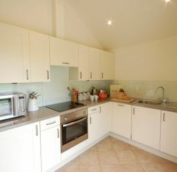 A kitchen with white cabinets a microwave oven a stove a kettle a teapot a bread bin and a sink at Remus Larling near East Harling