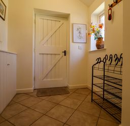 A hallway with a wooden door a tile floor a shoe rack and a window with a vase of flowers at Remus in Larling near East Harling