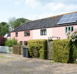 A pink house with solar panels on the roof a wooden gate and hedges in front at Seafarers in Fressingfield