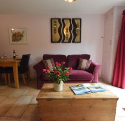 A living room with a purple sofa wooden coffee table with flowers and an open book and a dining table with chairs at Seafarers in Fressingfield