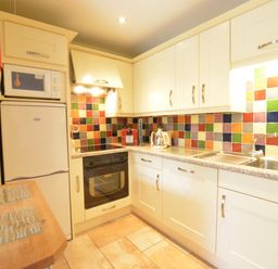 A kitchen with white cabinets colorful tiled backsplash oven microwave fridge and double sink at Seafarers in Fressingfield