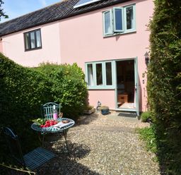 A small courtyard with a metal table and chairs and an open door to a pink house at Seafarers in Fressingfield