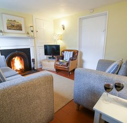 A living room with a fireplace two grey sofas a small table with wine and glasses and a leather chair at Aldeburgh Cottage in Aldeburgh