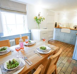 A kitchen with a wooden dining table set for four with wine and salad bowls next to blue cabinets and a white smeg fridge at Aldeburgh Cottage in Aldeburgh