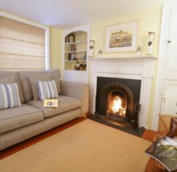 A living room with a sofa, fireplace with fire, TV, bookshelf, and a chair with an open magazine at Aldeburgh Cottage in Aldeburgh