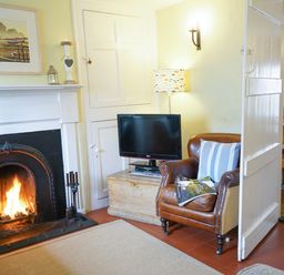 A living room with a fireplace a leather armchair a television and a wooden chest at Aldeburgh Cottage in Aldeburgh