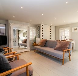 A living room with grey sofas a large decorative mirror a small dining table and white shutters at Mariners Cottage in Aldeburgh