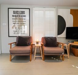A sitting area with two armchairs a small table with a lamp and a wall-mounted television at Mariners Cottage in Aldeburgh