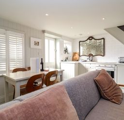 A kitchen and dining area with a table and chairs and a sofa with pillows at Mariners Cottage in Aldeburgh