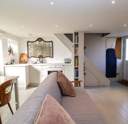An open plan kitchen and living area with a grey sofa and wooden dining chairs at Mariners Cottage in Aldeburgh