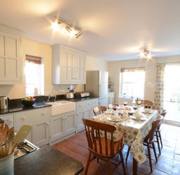 A kitchen with white cabinets a dining table set for six and a door opening to a garden at Pebble Beach Cottage Aldeburgh