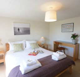 A bedroom with a double bed bedside tables lamps a wooden desk chair and a large mirror at Pebble Beach Cottage Aldeburgh